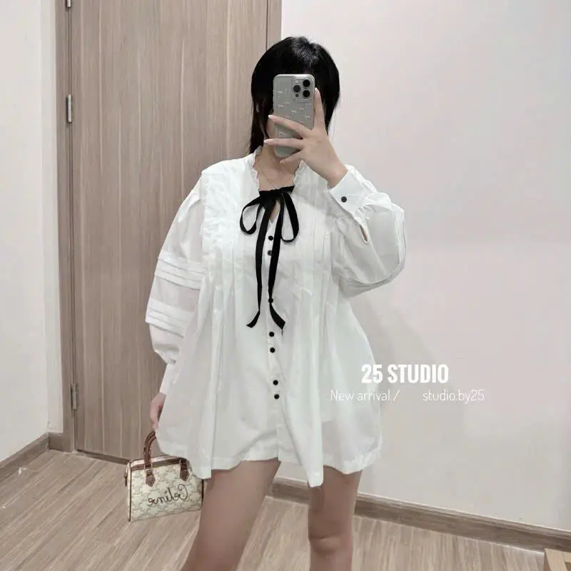 Áo sơ mi nữ trắng kiểu dáng oversize, thiết kế tay dài bo chun, cổ tròn viền bèo, có nơ đen sang chảnh, dễ phối đồ
